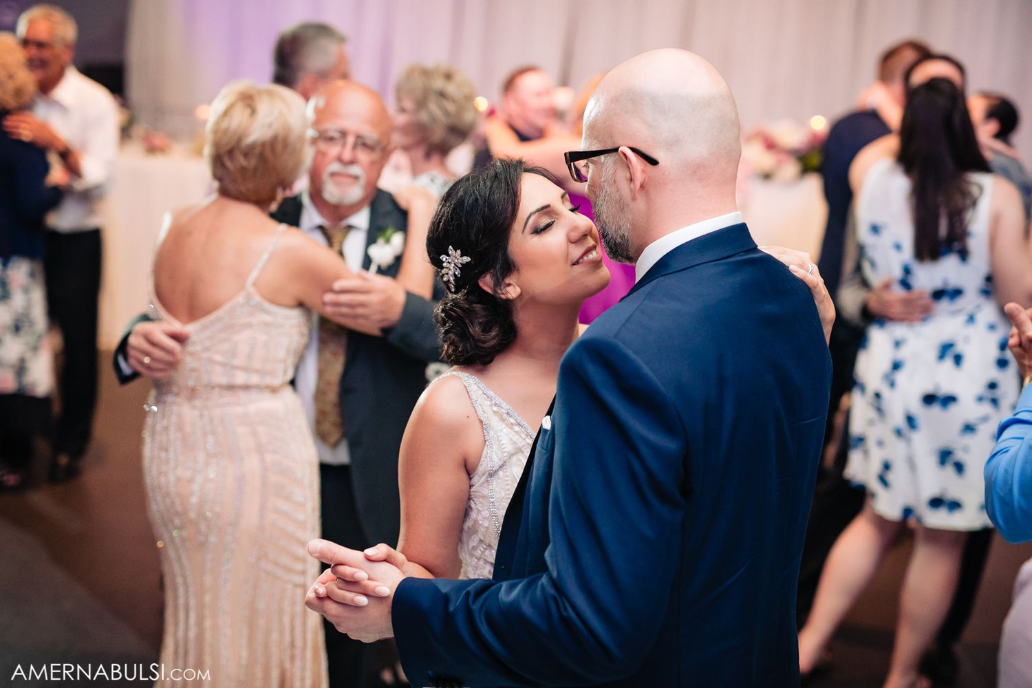 Couples slow dance together at an elegant wedding reception with soft lighting.