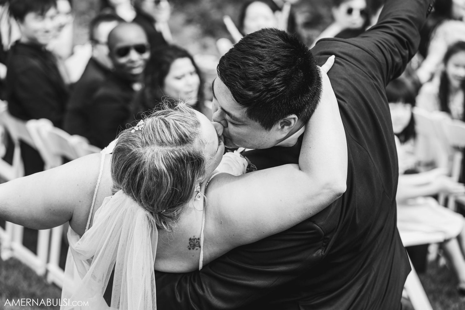 Black and white photo of newlyweds sharing romantic kiss during ceremony.