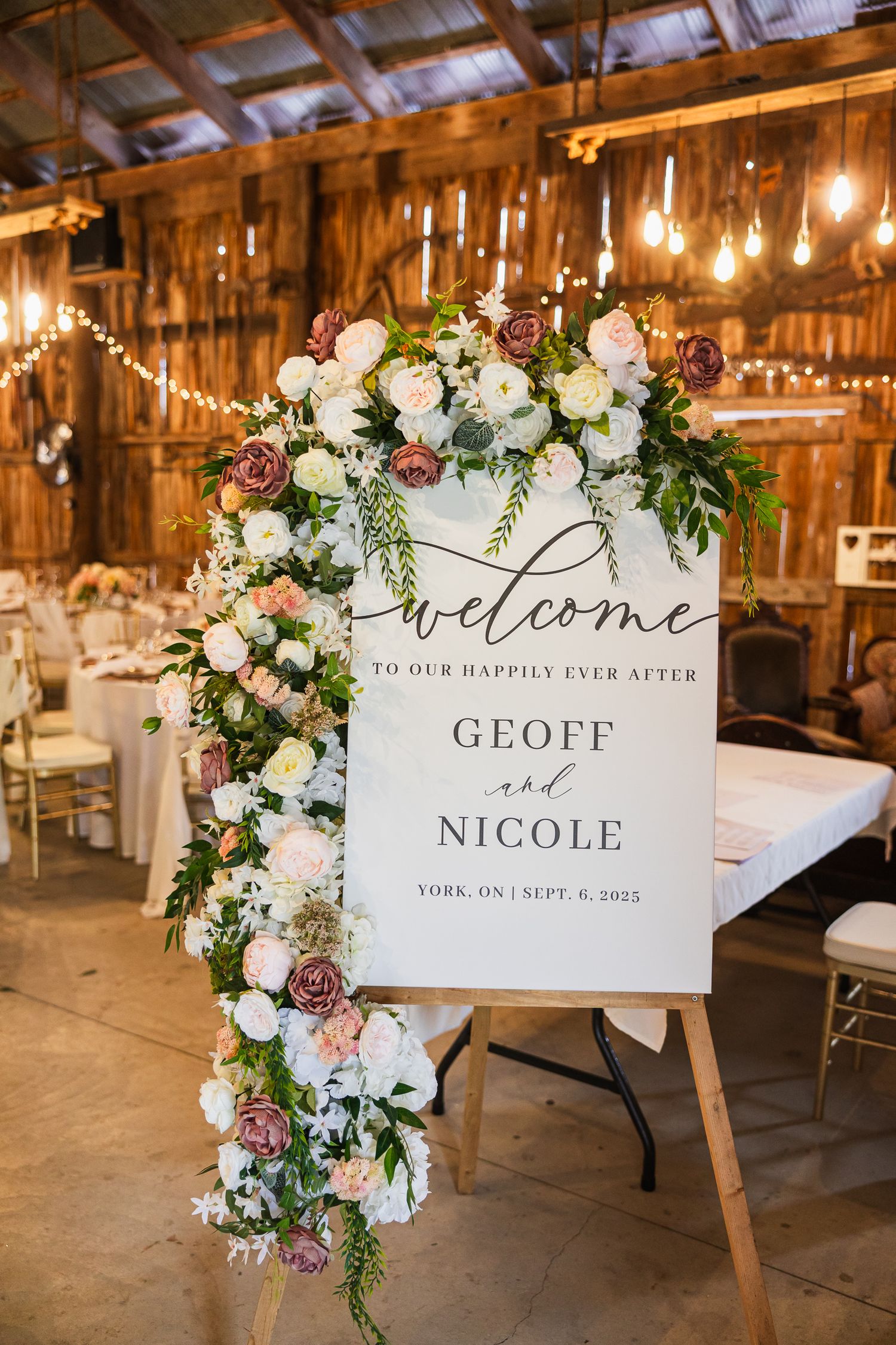 Rustic barn wedding reception with welcome signs and floral decorations displayed on wooden easels.