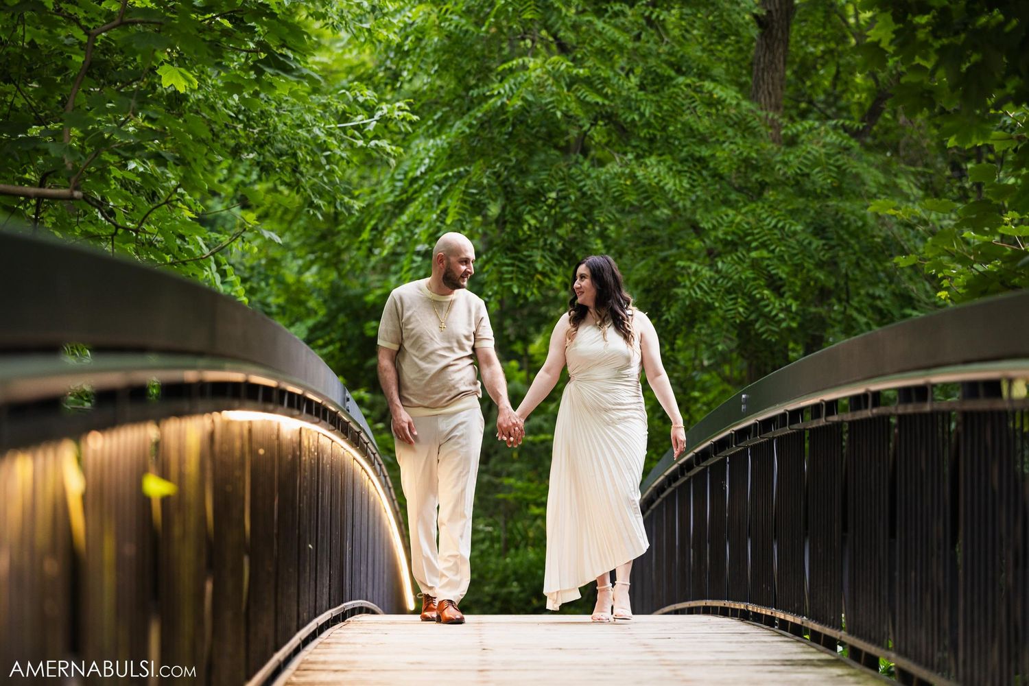 Couple walking together on a wooden bridge with sunlight filtering through trees.