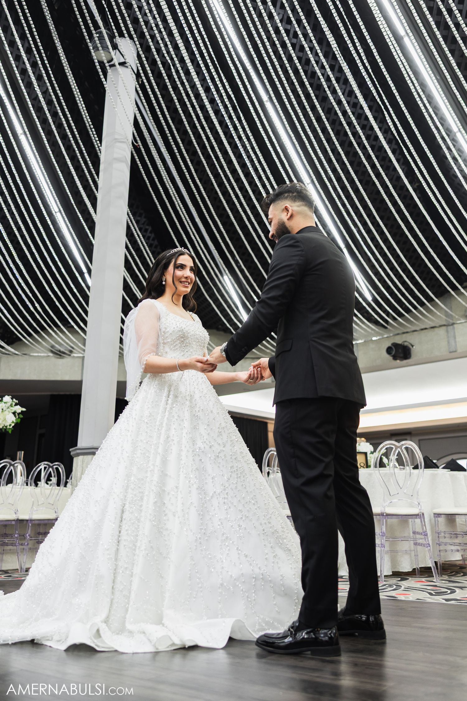 A bride in a flowing white gown dances with her partner on a modern dance floor under dramatic white draping.