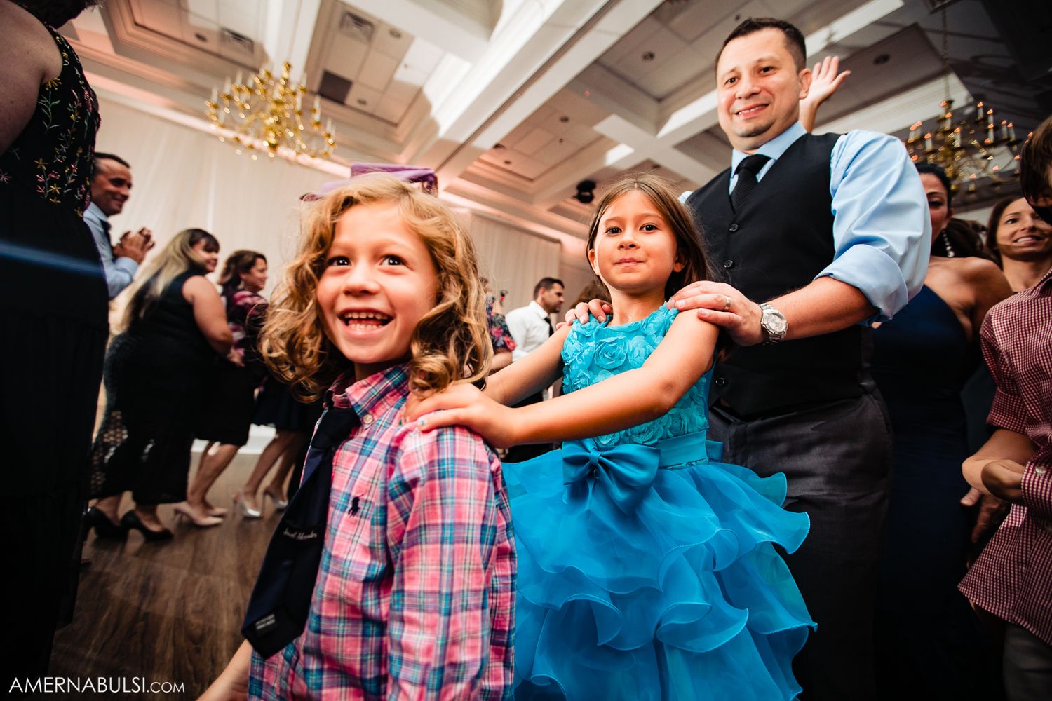 Wedding reception celebration showing joyful dancing and festivities under elegant chandelier lighting.