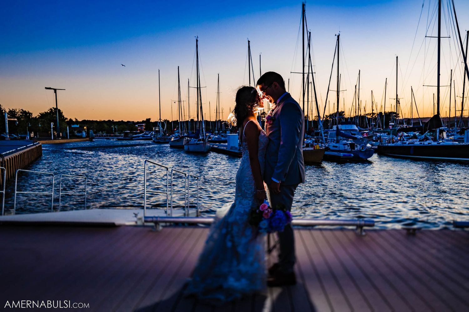 Romantic silhouette of couple embracing at marina during sunset with boats in background.