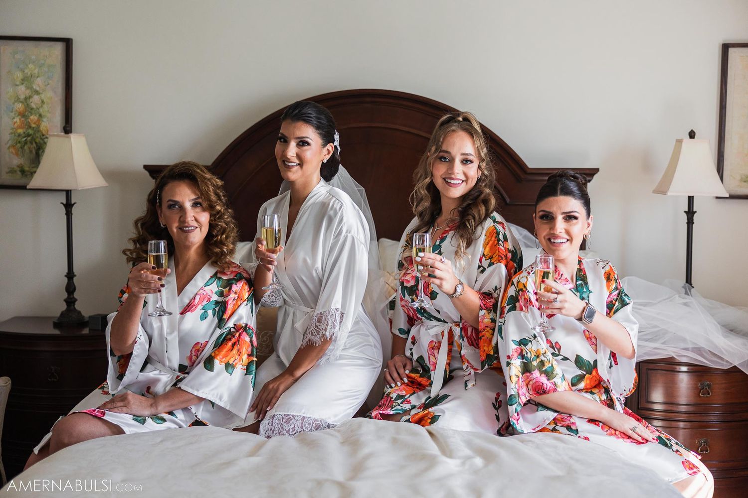 Four people in matching floral robes sit together on a bed during wedding preparations.