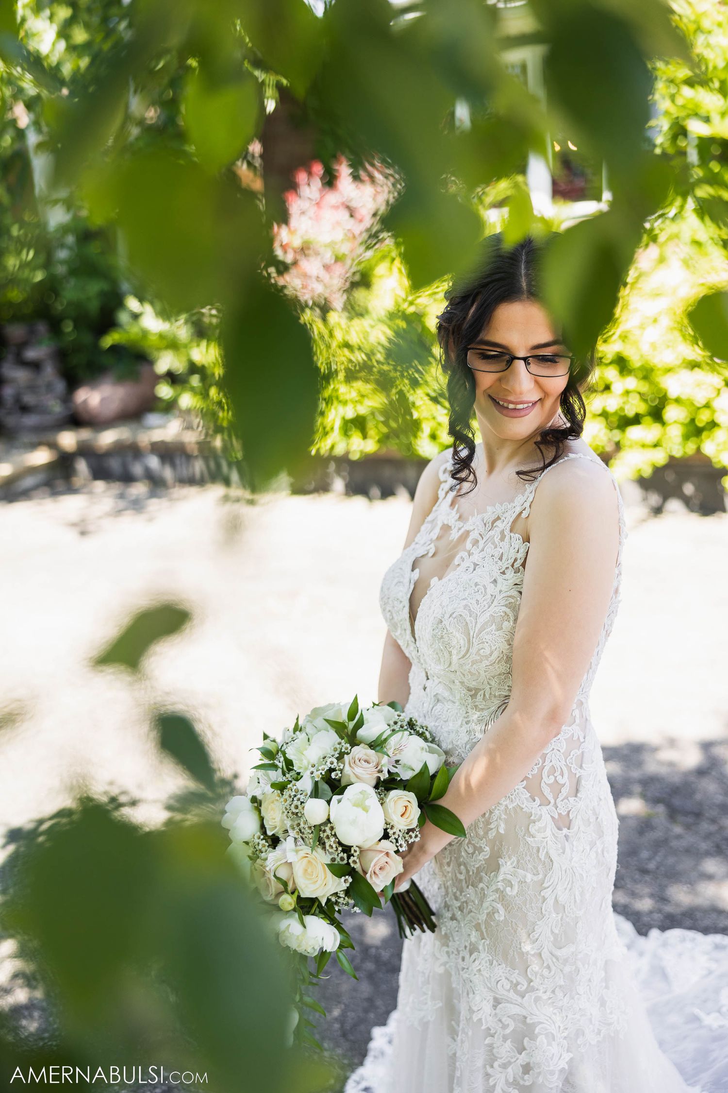 Summer garden bridal portrait with white floral bouquet through green leaves.