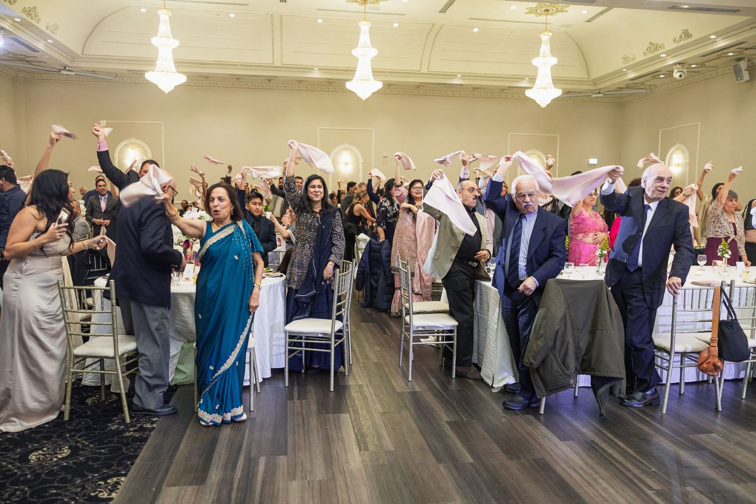 Wedding guests stand and cheer during celebration in elegant ballroom setting.