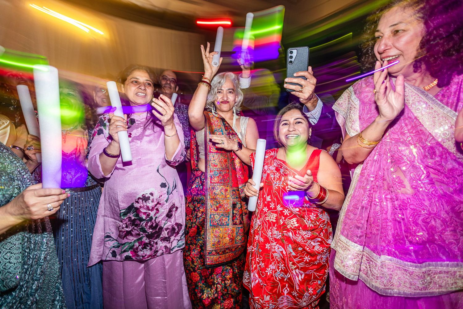 People dancing and celebrating at a nightclub with colorful purple and pink lighting effects illuminating the dance floor.