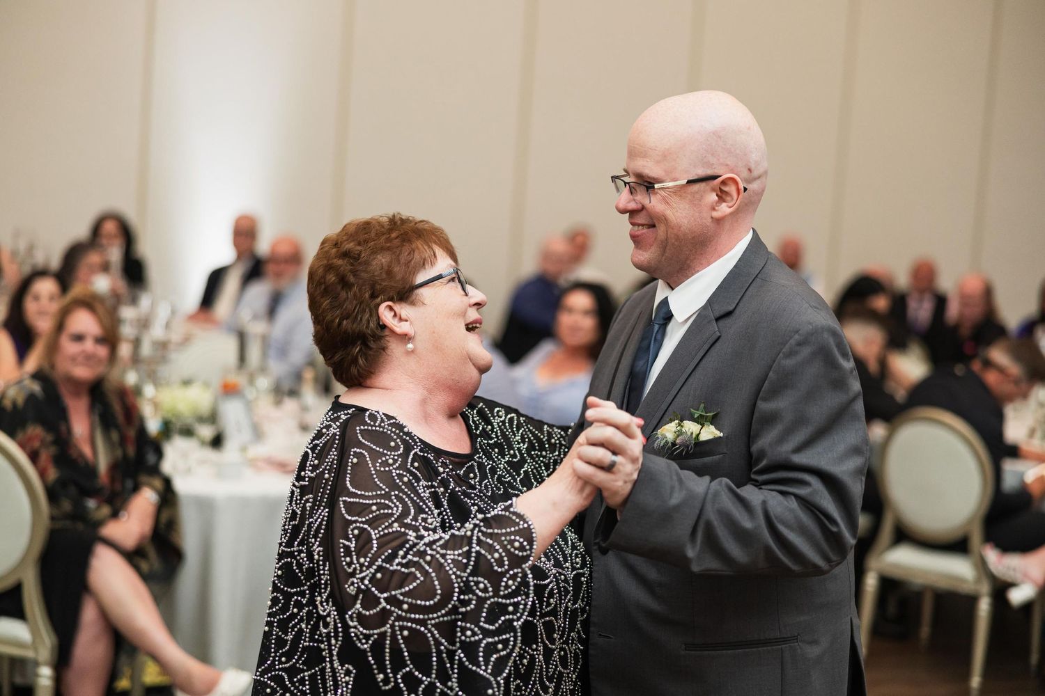 Candid moment of dancing couple at formal event venue with audience in background.