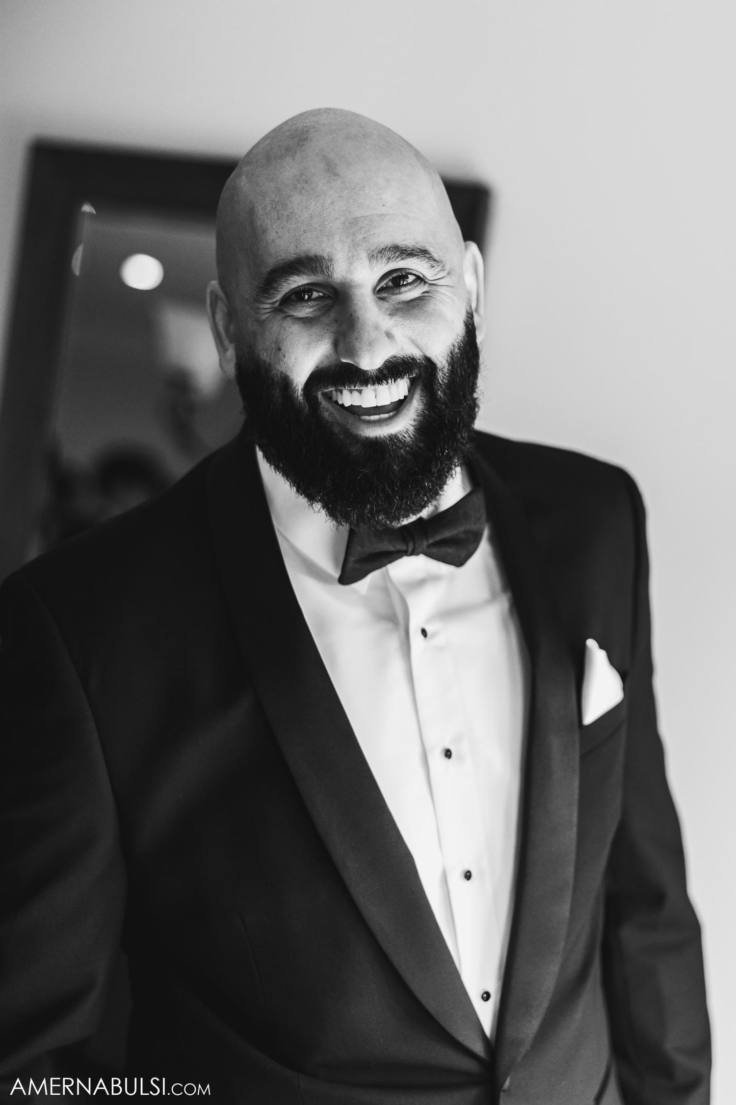 Black and white portrait of person in tuxedo with full beard smiling warmly.