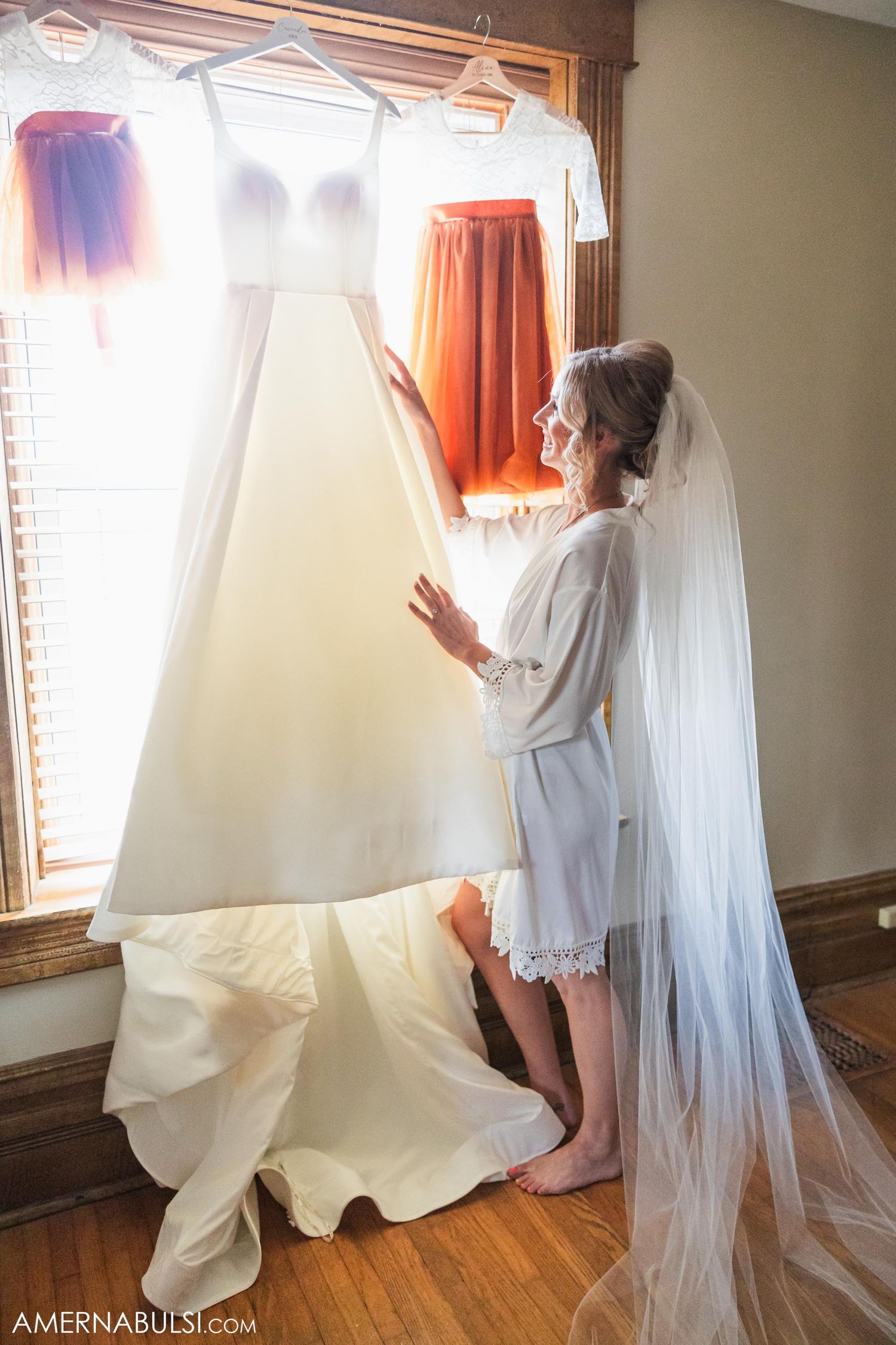 A wedding dress and veil hanging by a window in natural sunlight.