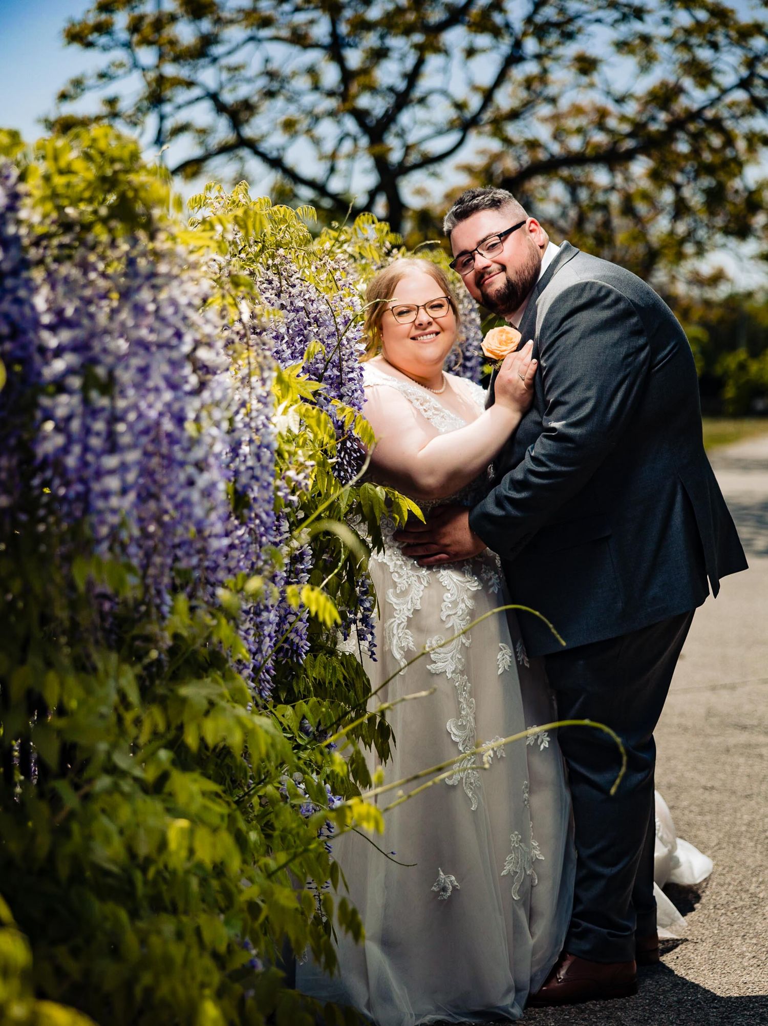 Couple shares intimate moment by blooming wisteria during spring wedding.
