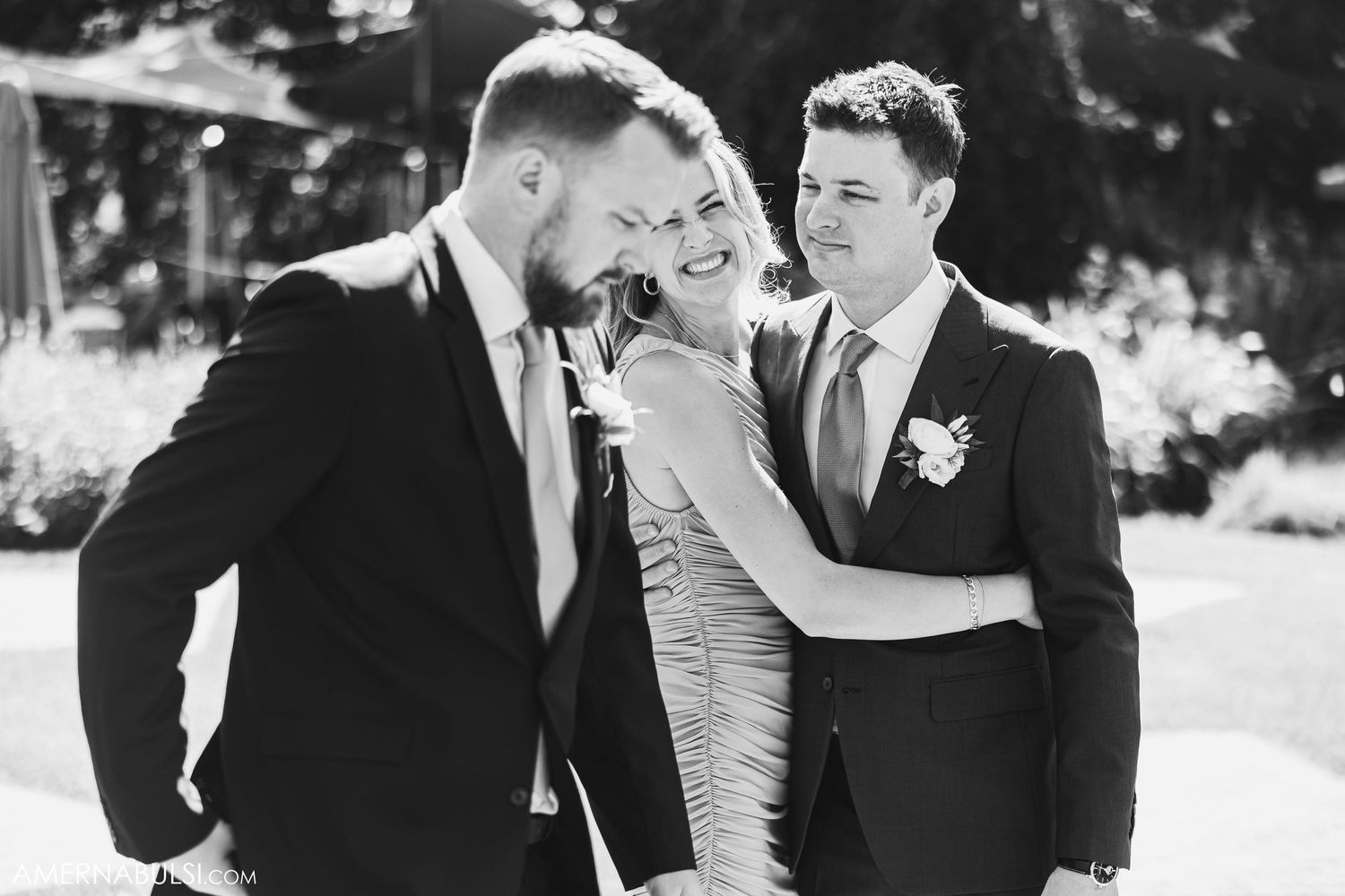 Wedding party shares a candid laughing moment together outdoors in black and white.