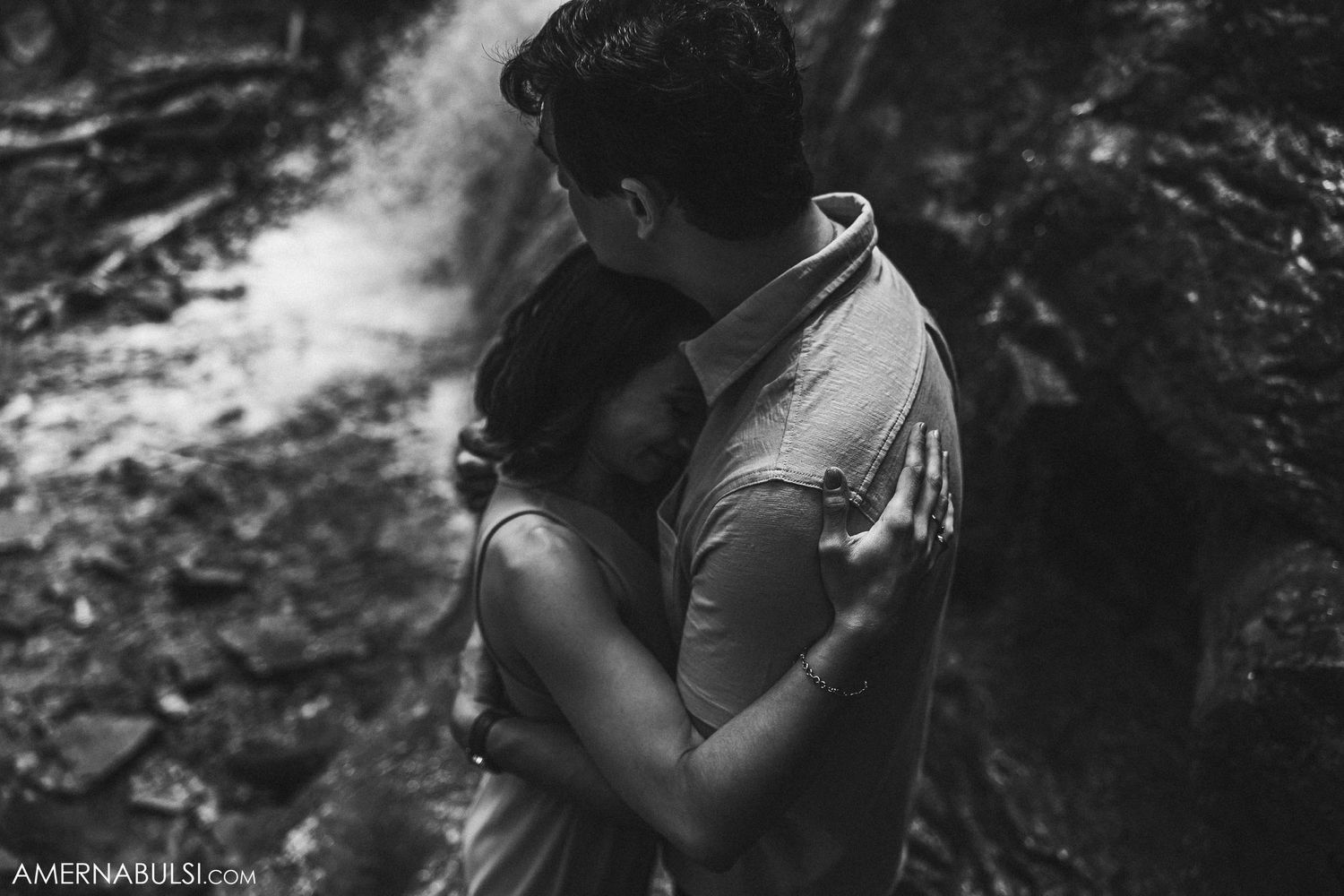 Intimate black and white portrait of couple embracing near rocky outcrop.