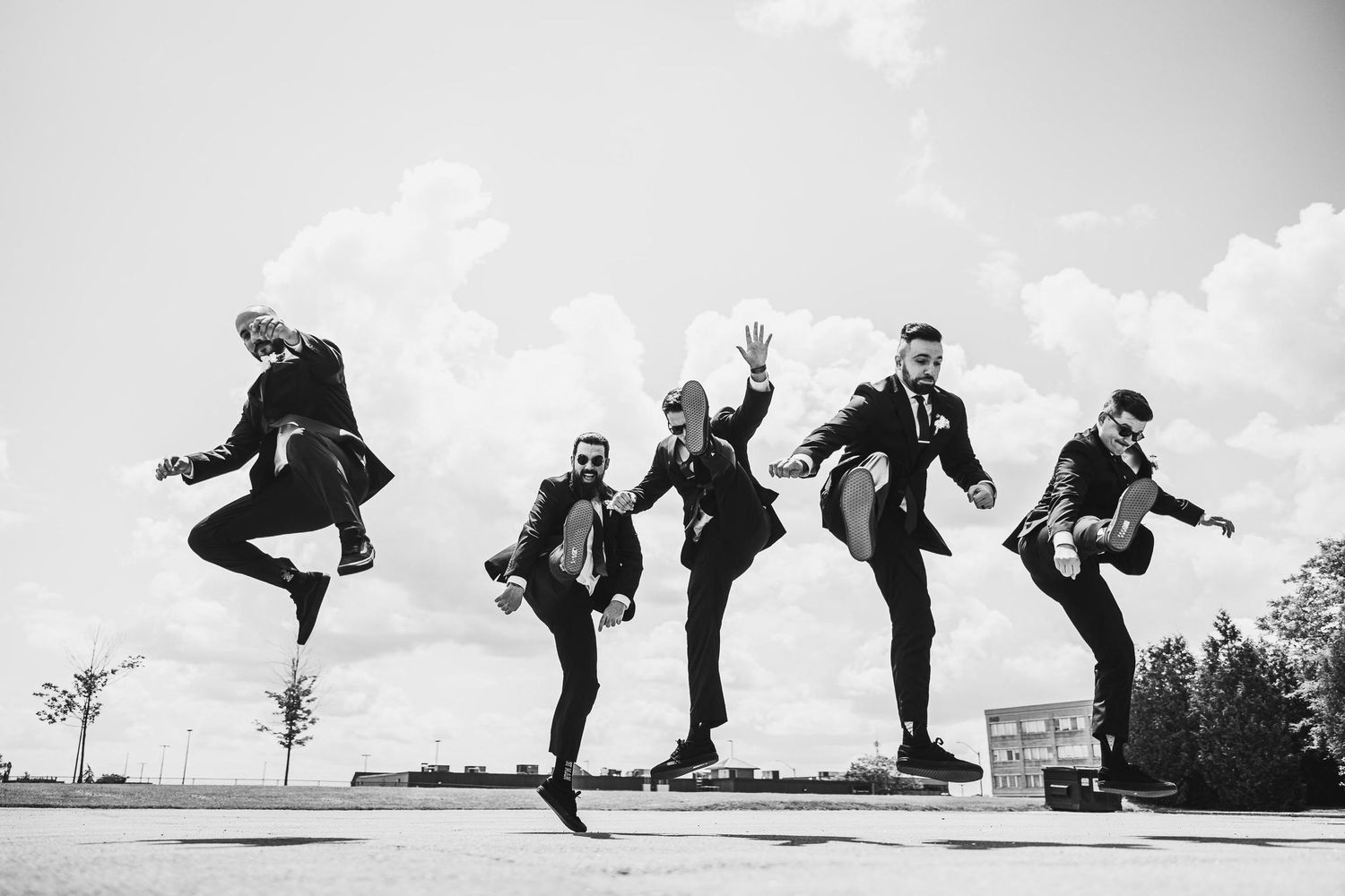Groomsmen in suits performing synchronized jumping pose outdoors in black and white photography.