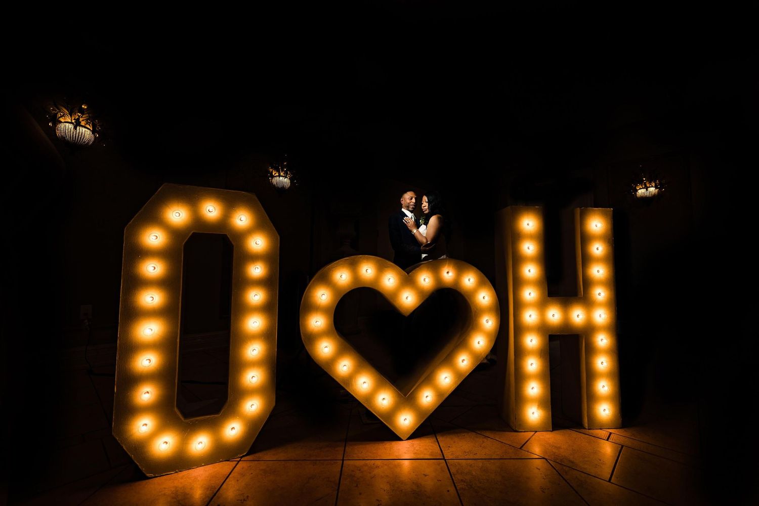 Illuminated marquee letters spelling 'OH' with a glowing heart symbol in the middle against a dark background.