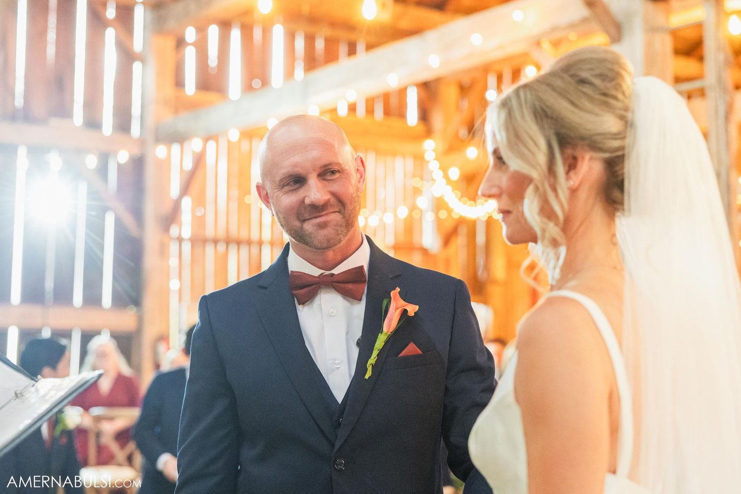 Groom in navy suit with bow tie during rustic barn wedding ceremony.