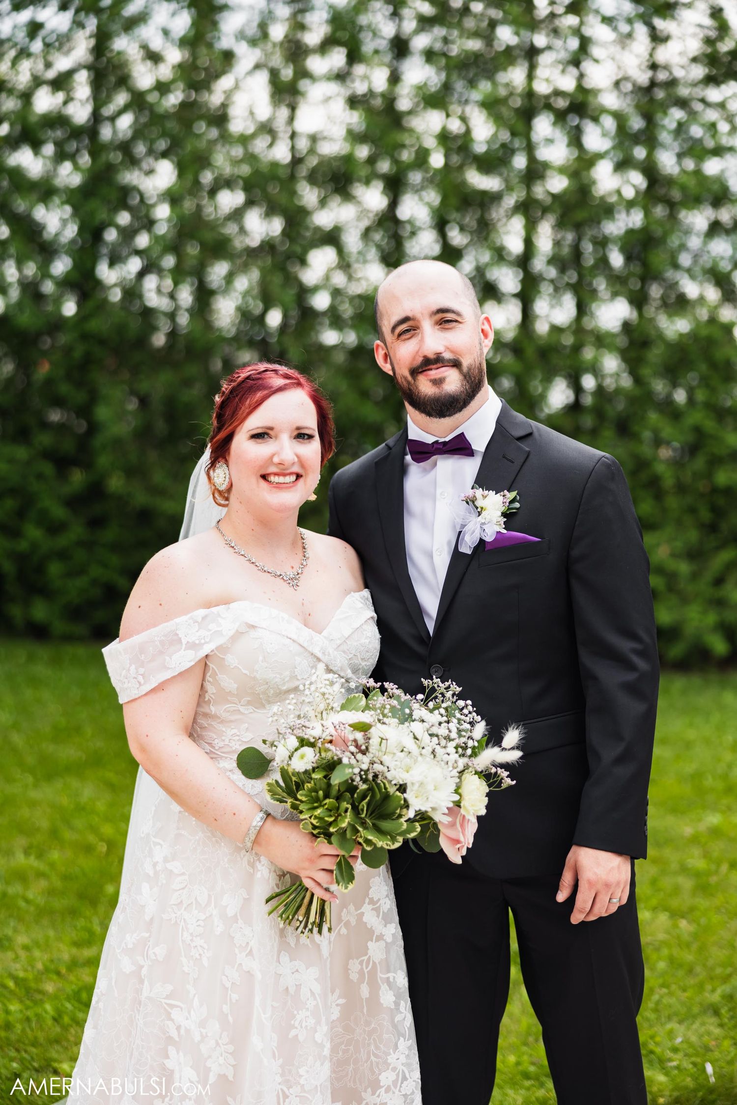 Newlyweds pose for a formal portrait outdoors holding a white floral bouquet.