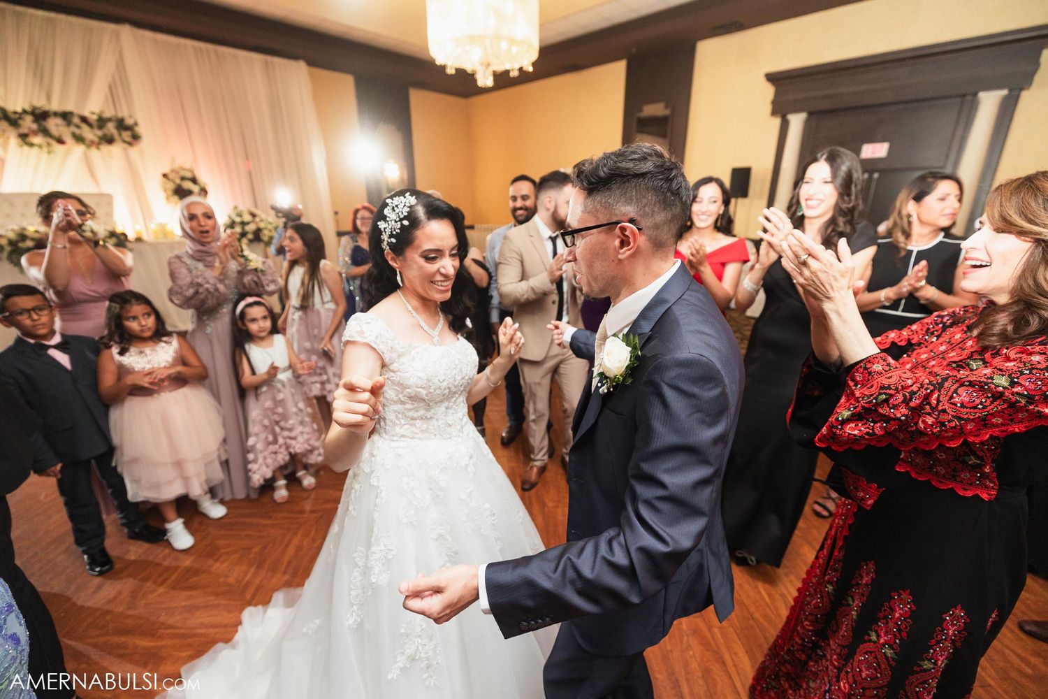 Newlyweds dancing together surrounded by cheering wedding guests in a beautifully decorated reception hall.