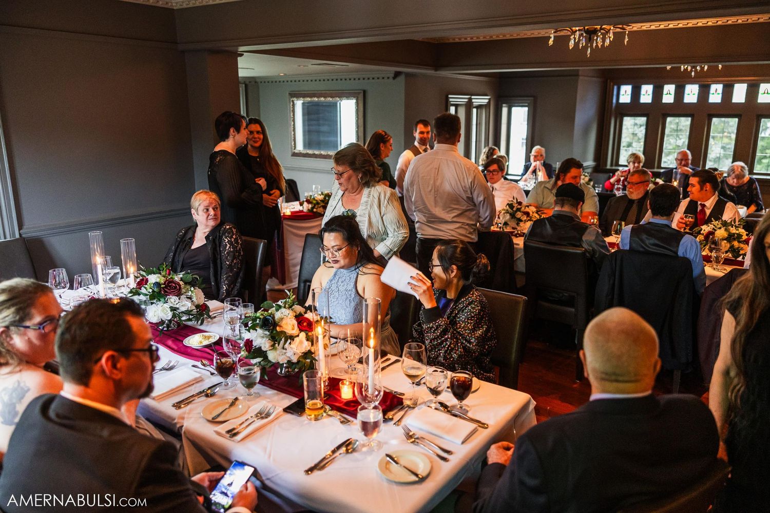 Wedding reception dining room filled with guests at long tables with burgundy decor.