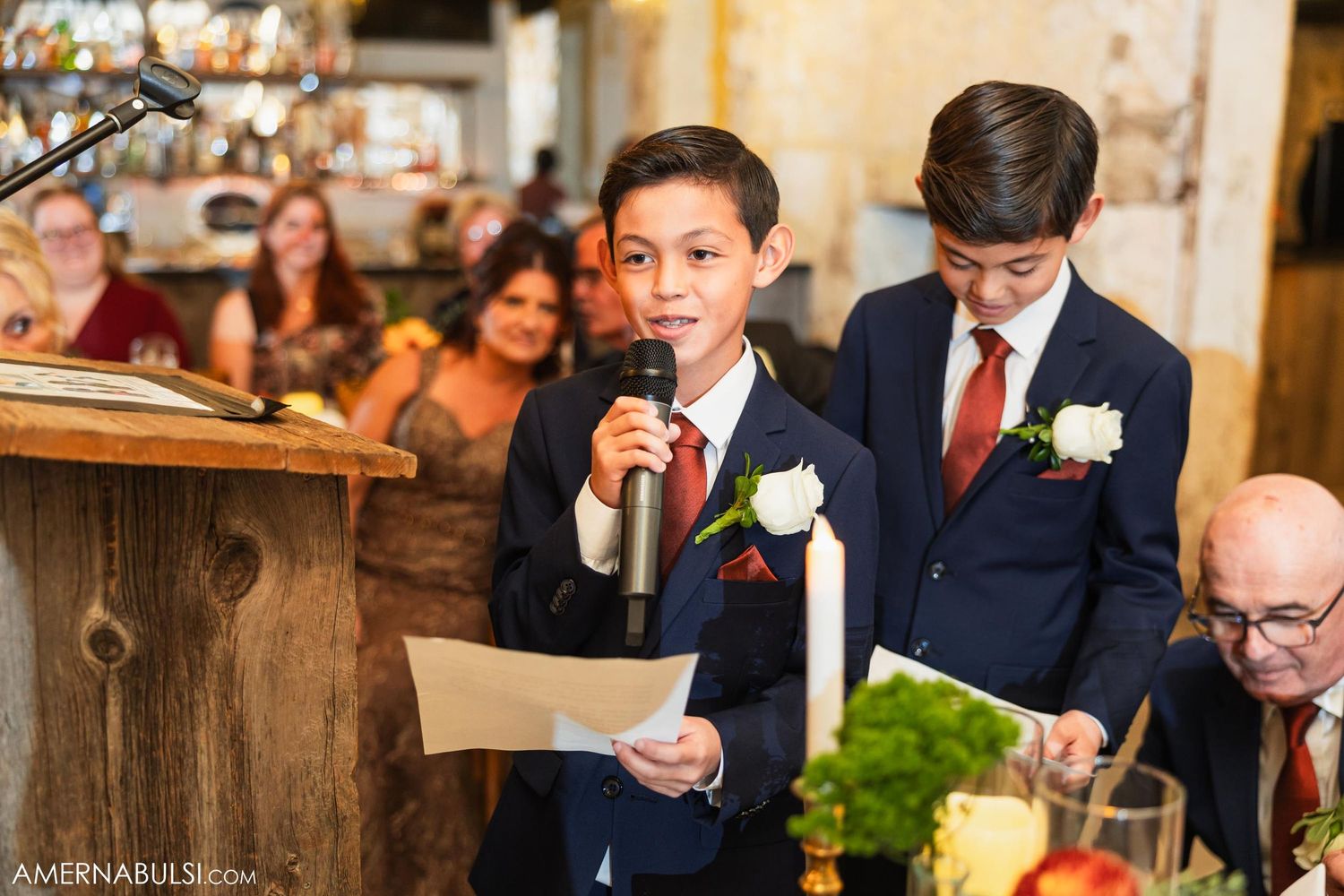 Young groomsmen deliver speeches at wedding reception while holding microphone.
