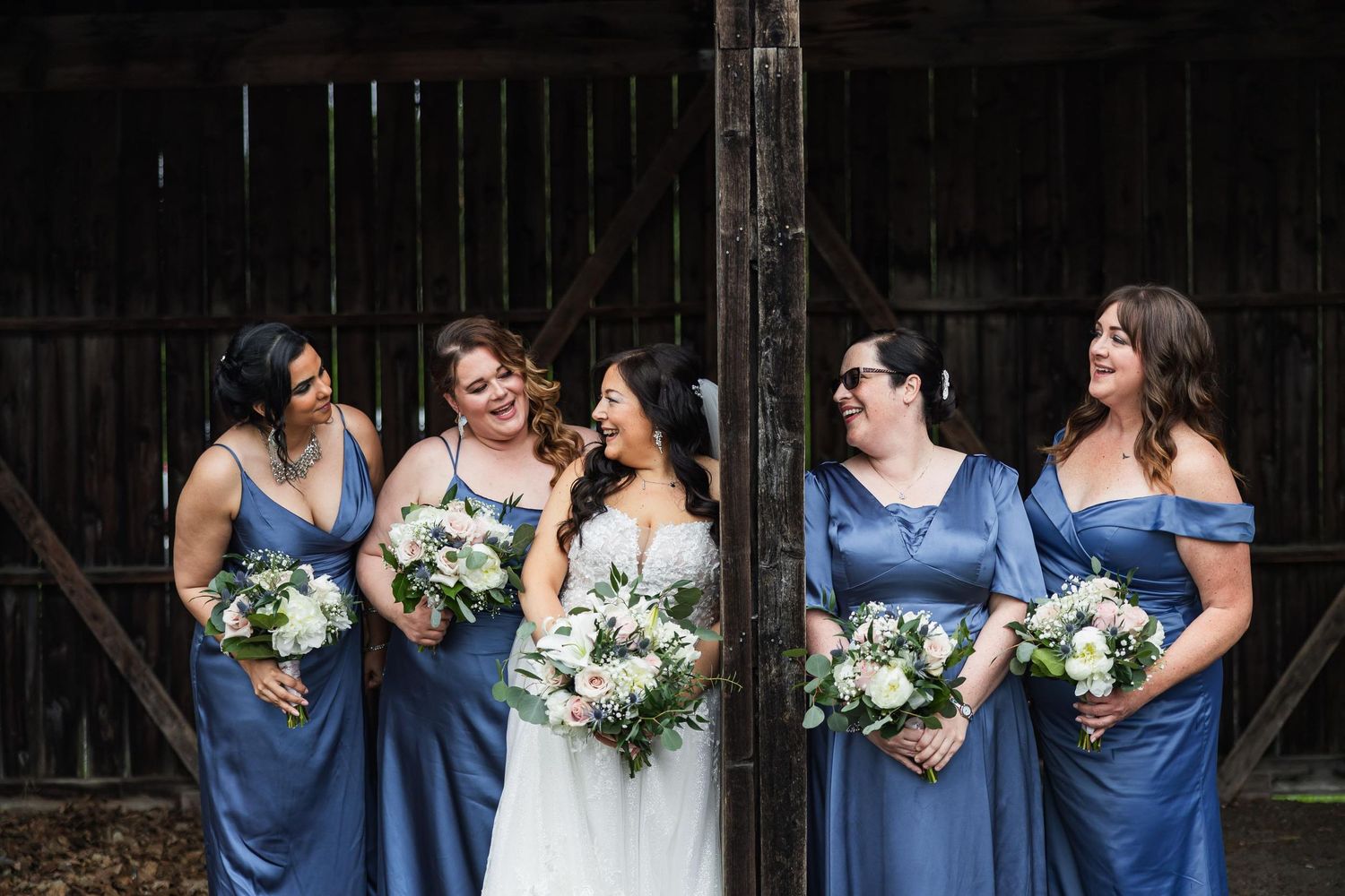 Wedding party poses inside rustic barn with bridesmaids in blue dresses.