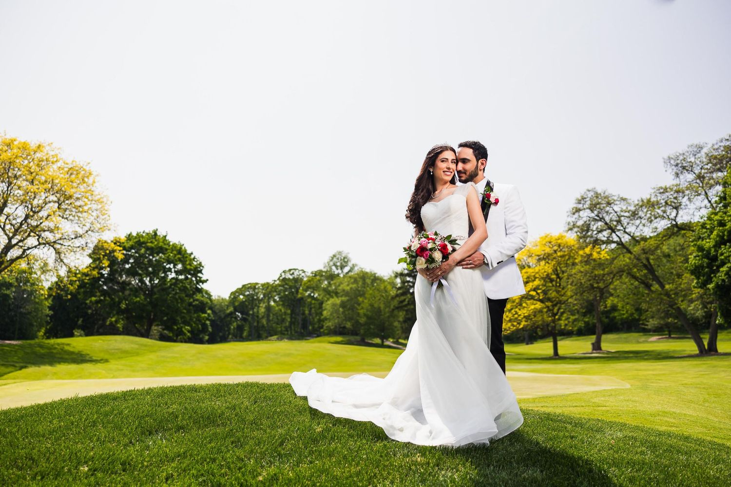 Newlyweds pose together on lush golf course during their wedding day.
