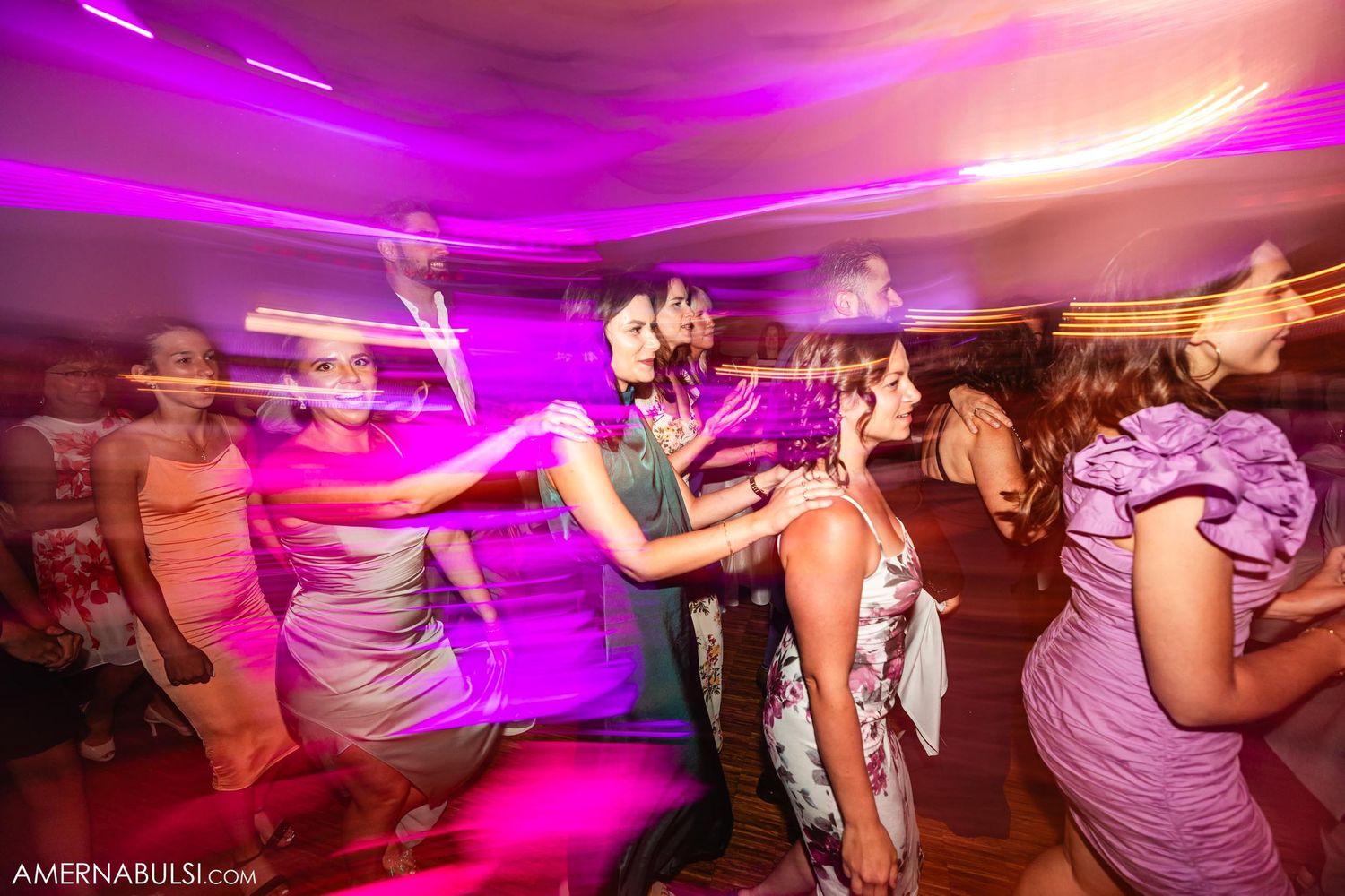 Party guests dancing energetically under bright magenta lighting at a wedding reception.