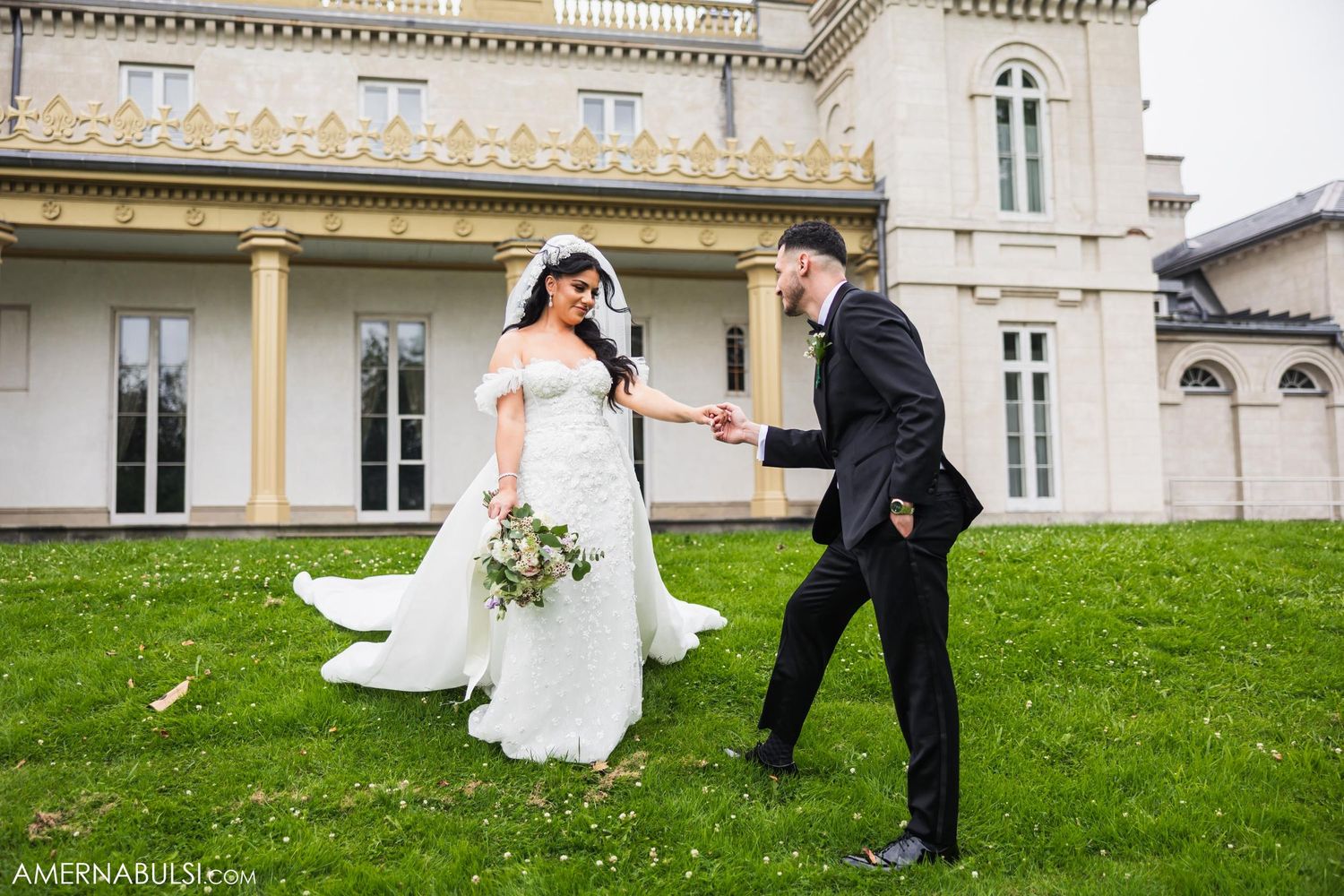 Wedding couple dancing joyfully on the lawn of a grand historic mansion with classical architecture.