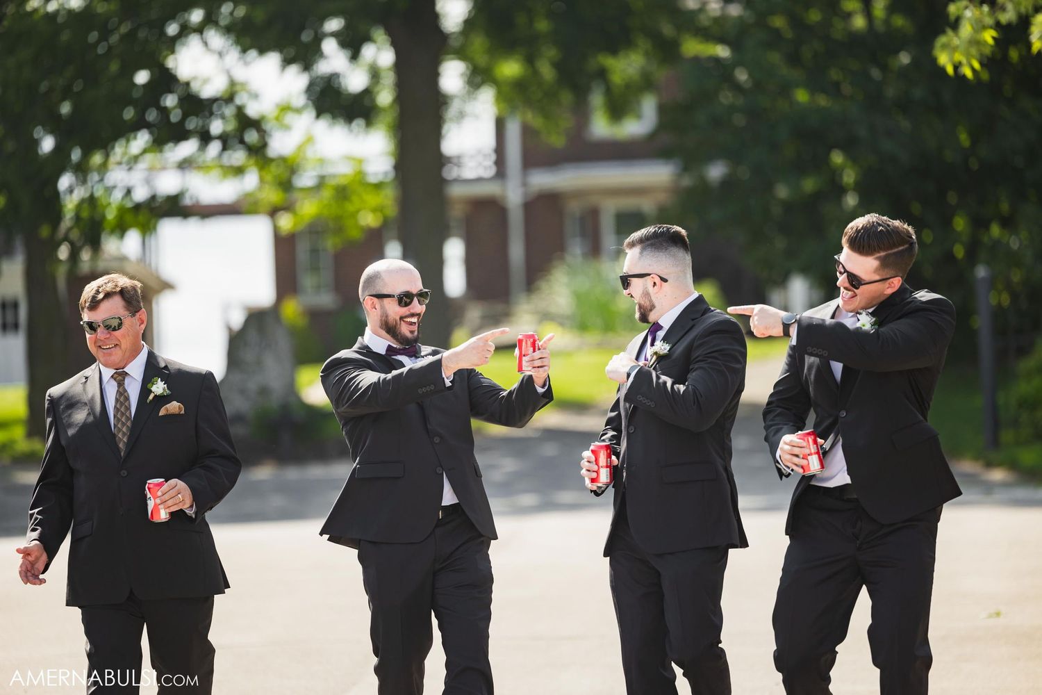 Groomsmen in black suits dancing and celebrating outdoors.