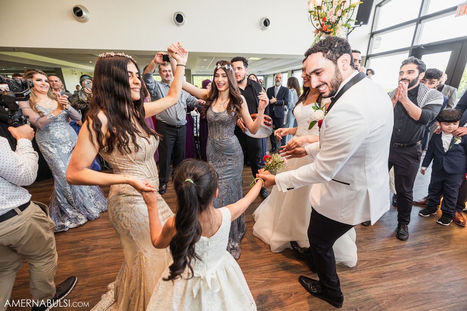 Wedding party dances energetically during reception celebration on hardwood dance floor.