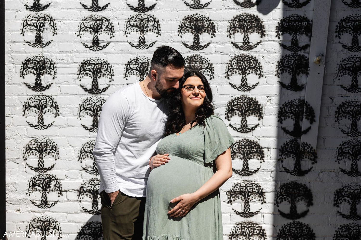 A maternity photo of a couple embracing against a patterned wall with tree designs.