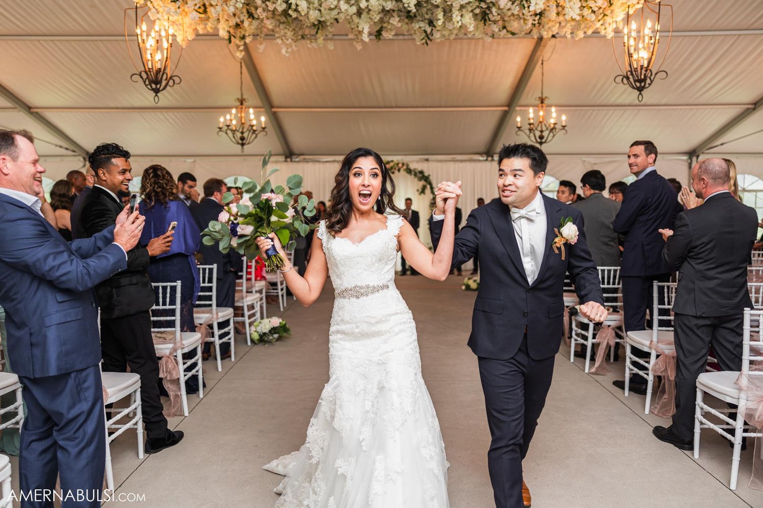 Wedding couple makes their grand exit down the aisle in an elegant white reception venue.