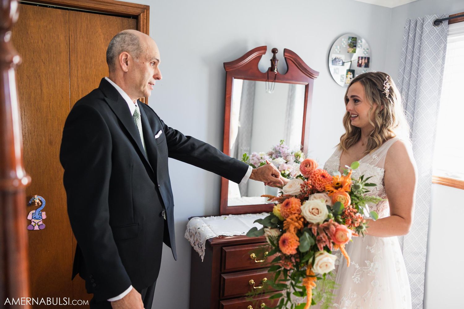 A tender wedding day interaction captured in a bedroom with coral flower bouquet.