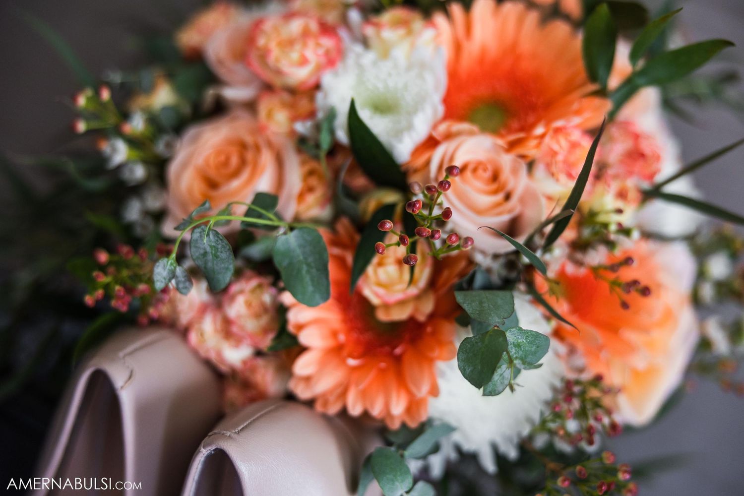Close-up of coral and peach wedding bouquet with roses and greenery.