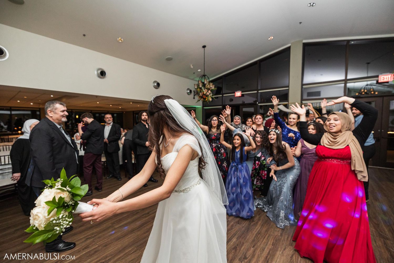 Wedding guests gather on a dance floor as a bouquet is tossed during the celebration reception.
