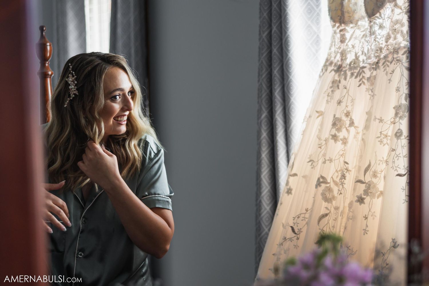 Contemplative moment captured as someone gazes at wedding dress hanging by window.