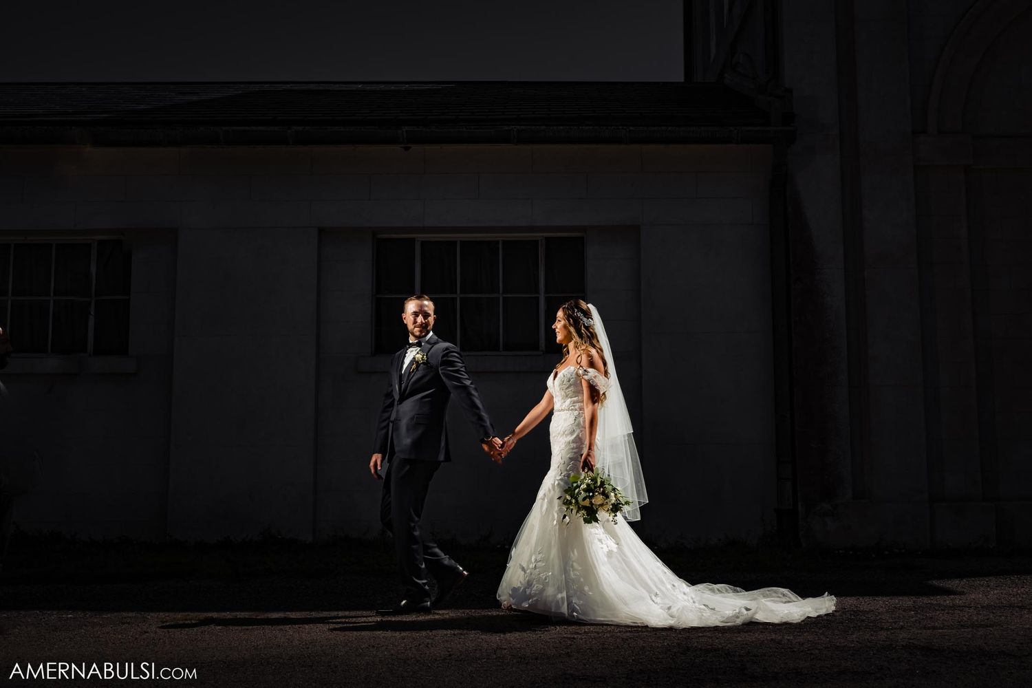 Dramatic backlit wedding portrait against dark building exterior.