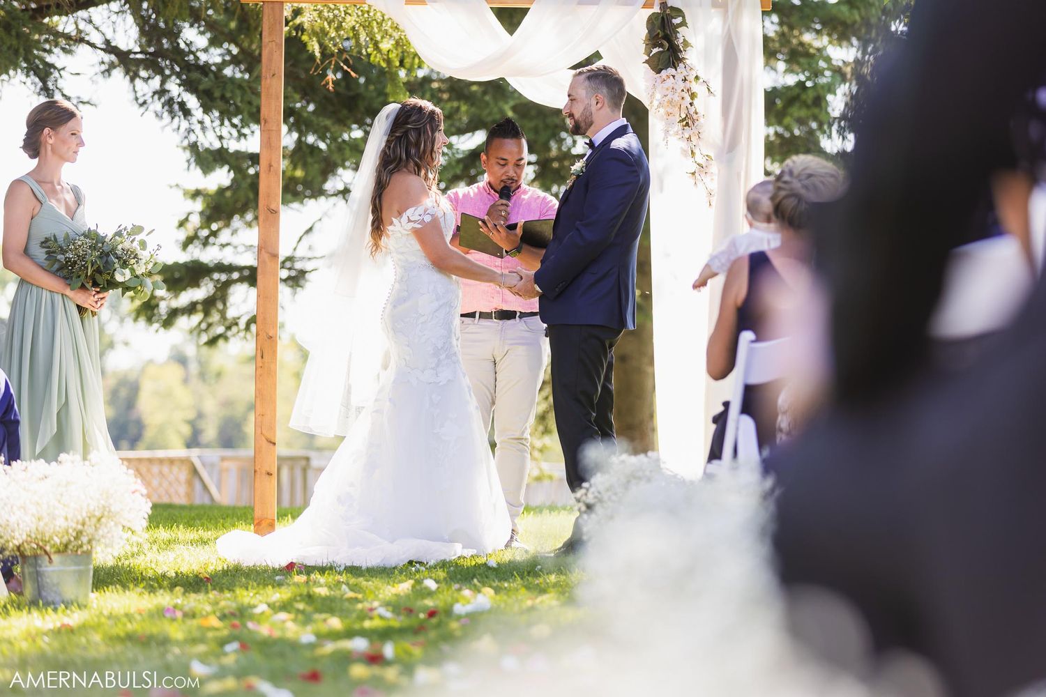 Outdoor wedding ceremony under white arch with scenic natural backdrop.
