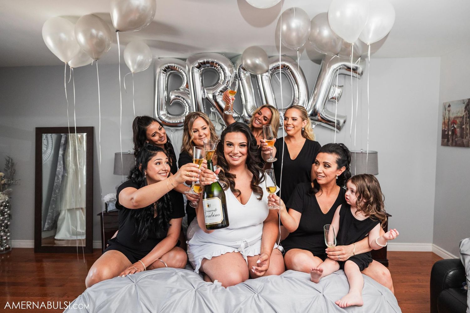Bridal party celebration with silver BRIDE balloons and champagne on bed.