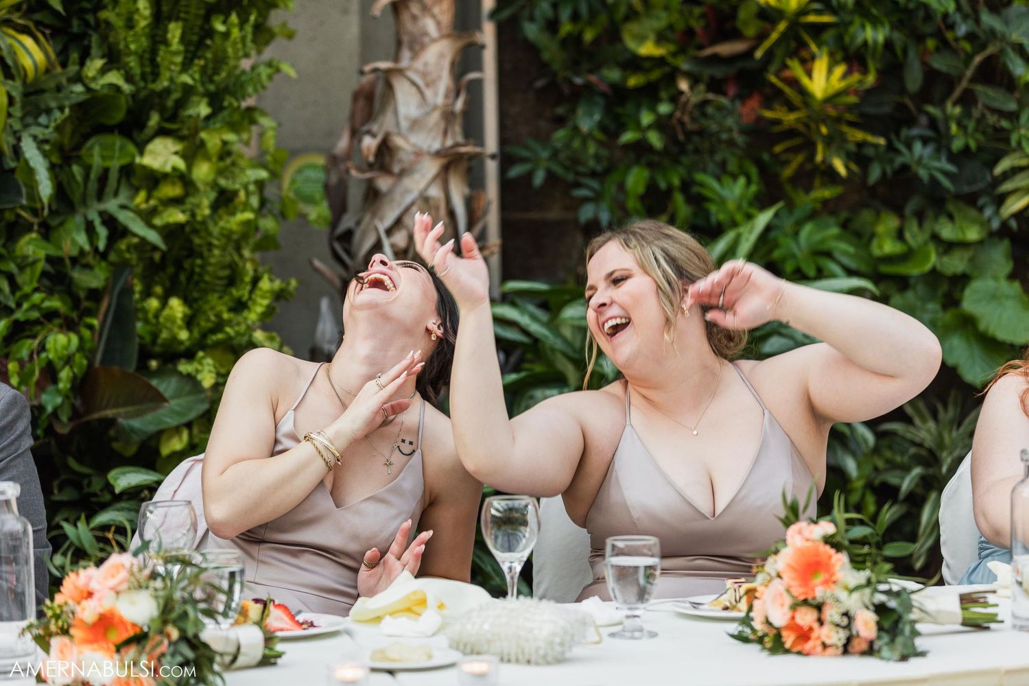 Wedding guests laugh heartily during an outdoor reception dinner.