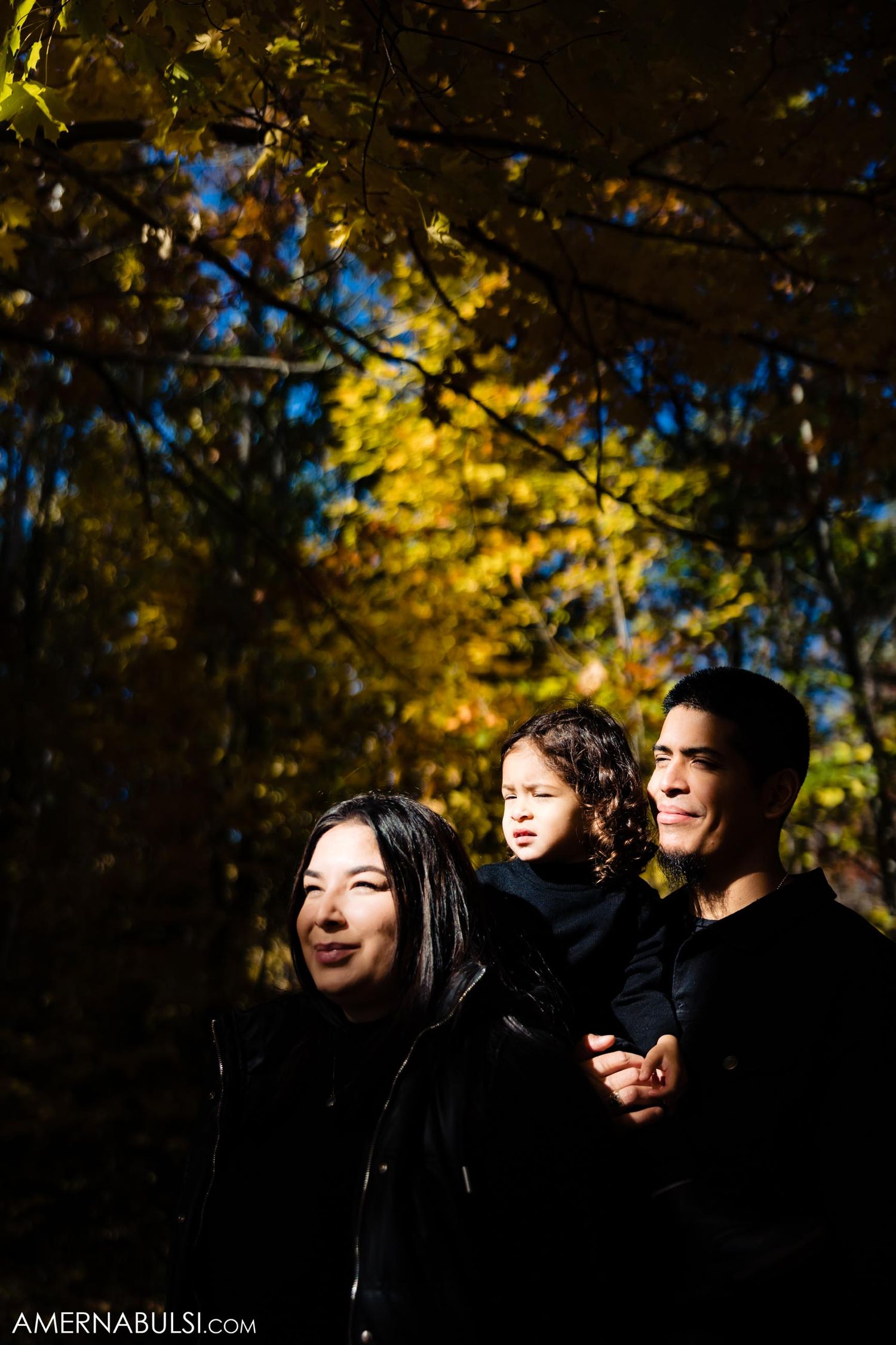 A candid autumn portrait captured in dramatic sunlight against colorful fall foliage.