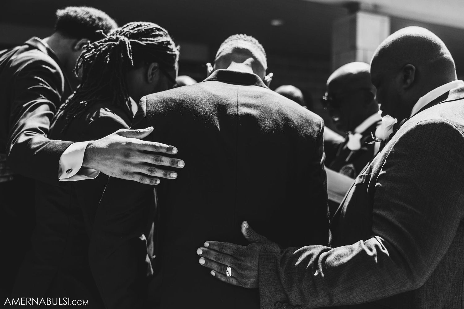 Black and white photo of groomsmen embracing in emotional moment.