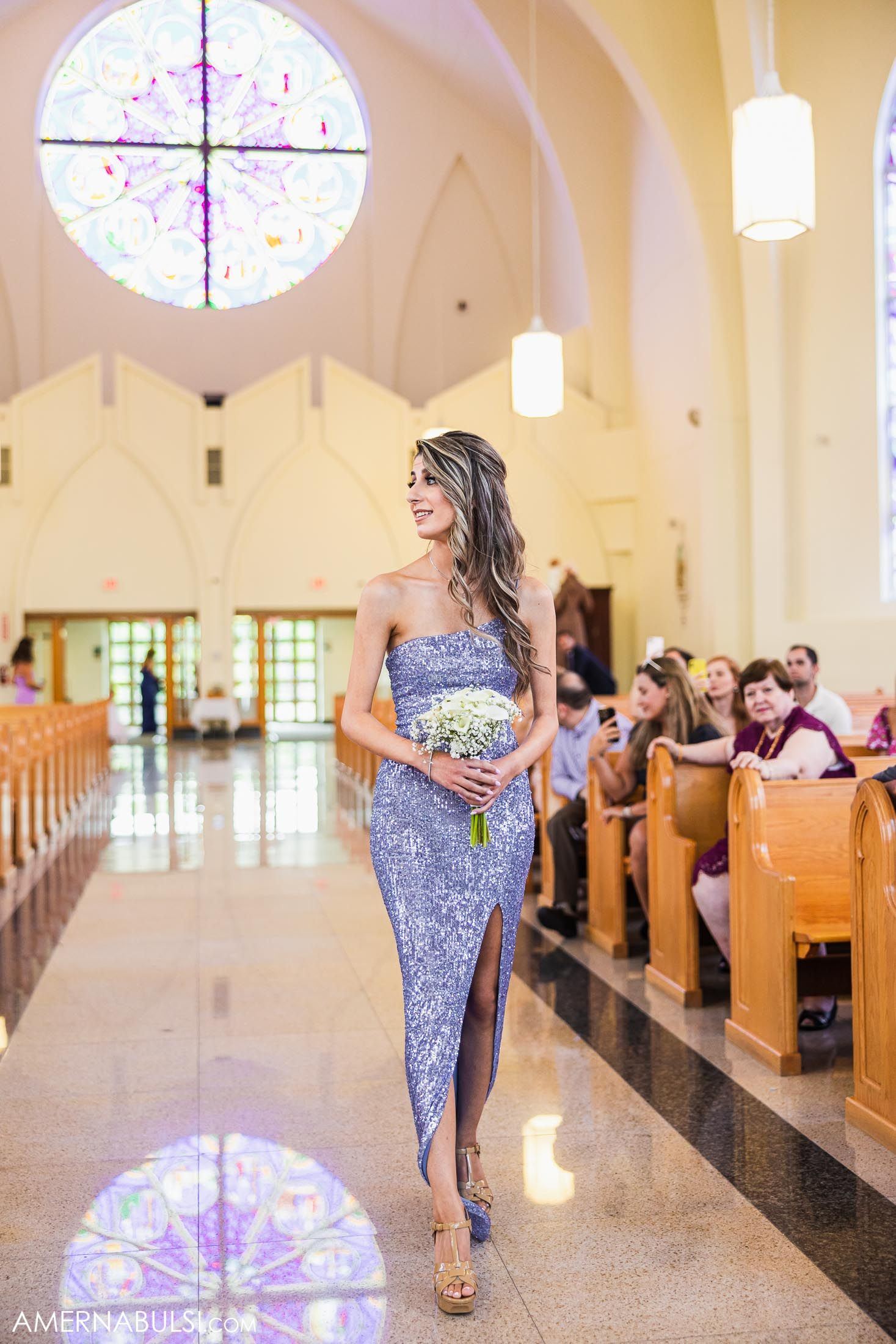 Bridesmaid in purple sequined dress walks down church aisle holding bouquet.