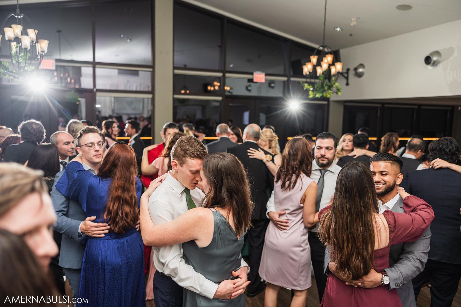 Couples dancing together on a crowded dance floor at an evening wedding reception.