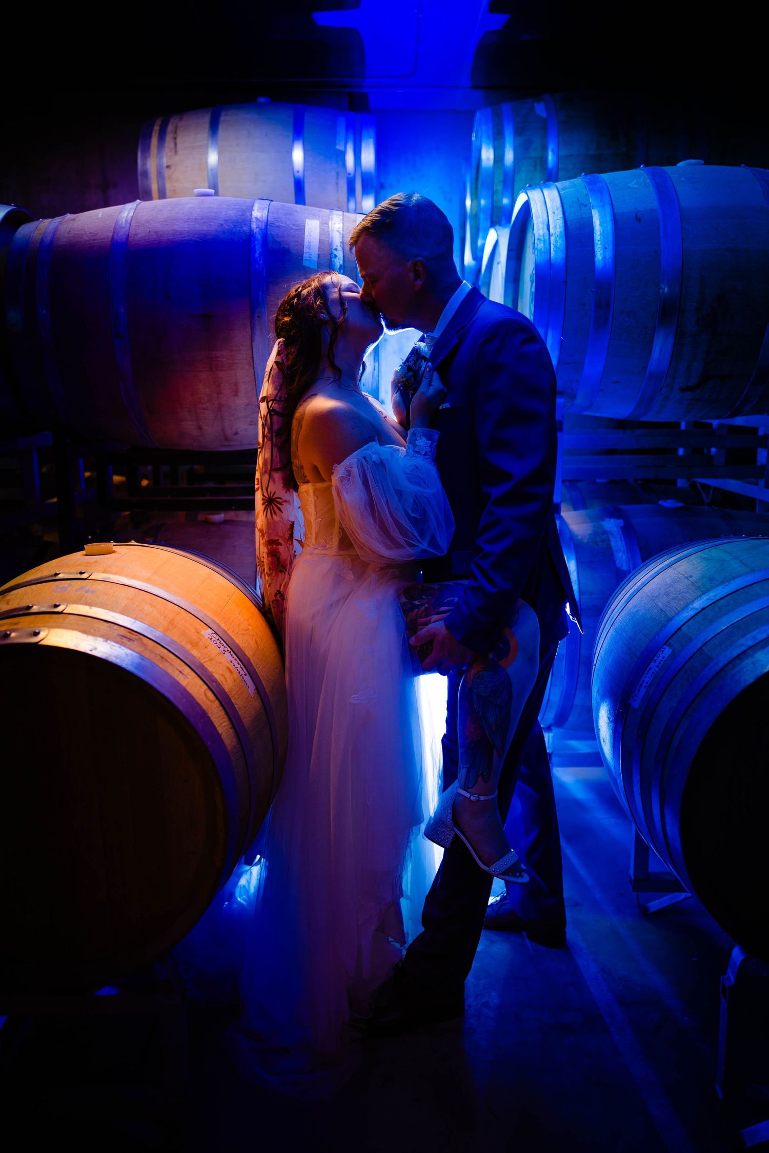 Atmospheric blue-lit wedding photos among wine barrels in cellar.
