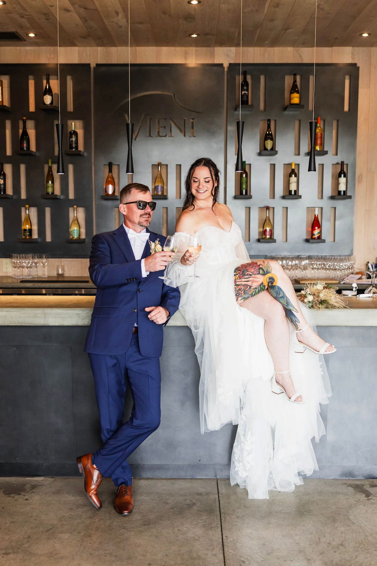 Couple shares drinks at modern wine bar with bottle display wall.