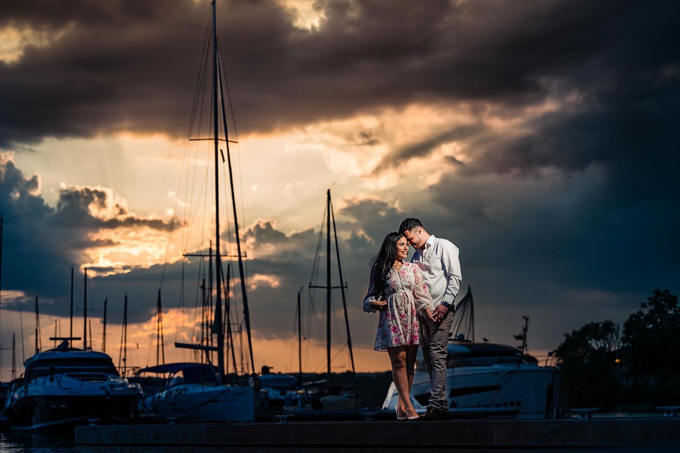 Marina at sunset with dramatic storm clouds and silhouetted sailboat masts.