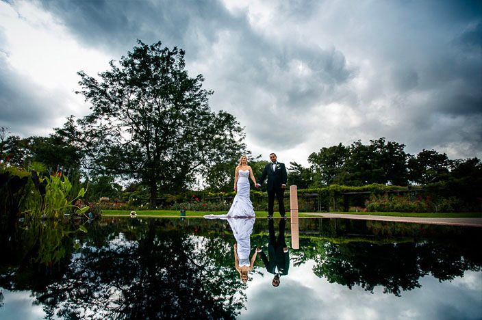 Dramatic wedding photos captured at sunset across a serene lake with reflections and trees in the background.