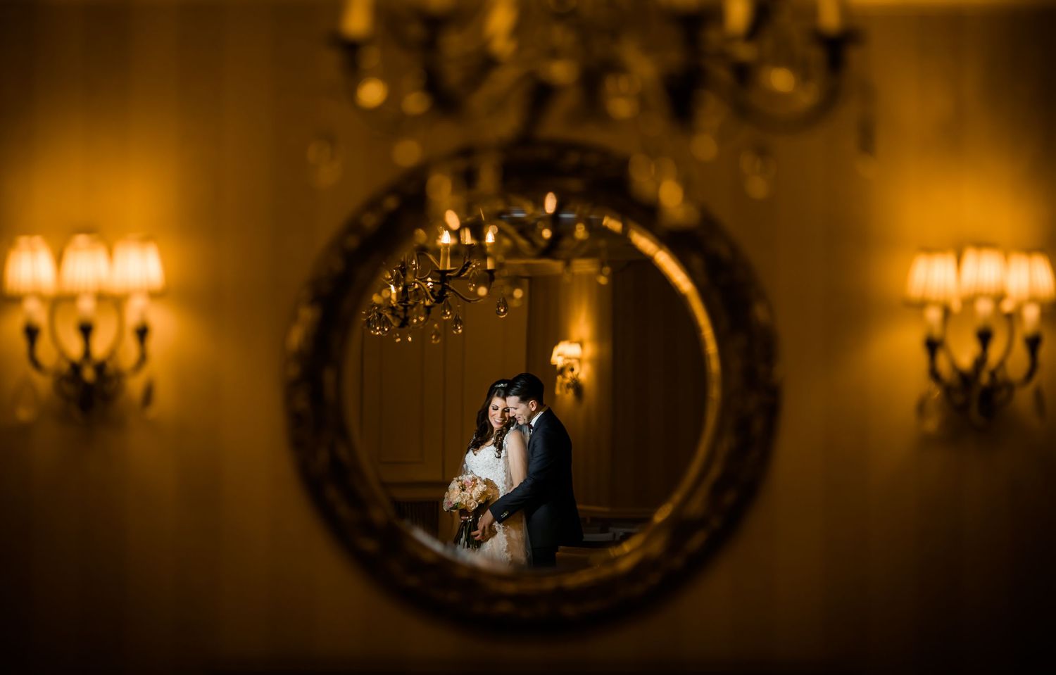 Romantic wedding portrait in warm lighting with ornate mirror and wall sconces.