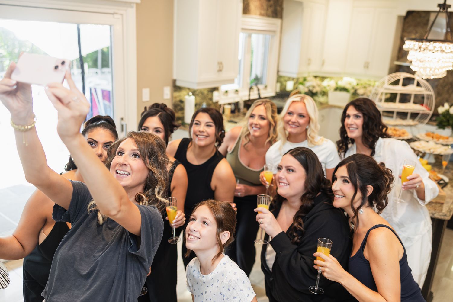 Group of bridesmaids taking a selfie while holding champagne glasses during a bridal party celebration indoors.